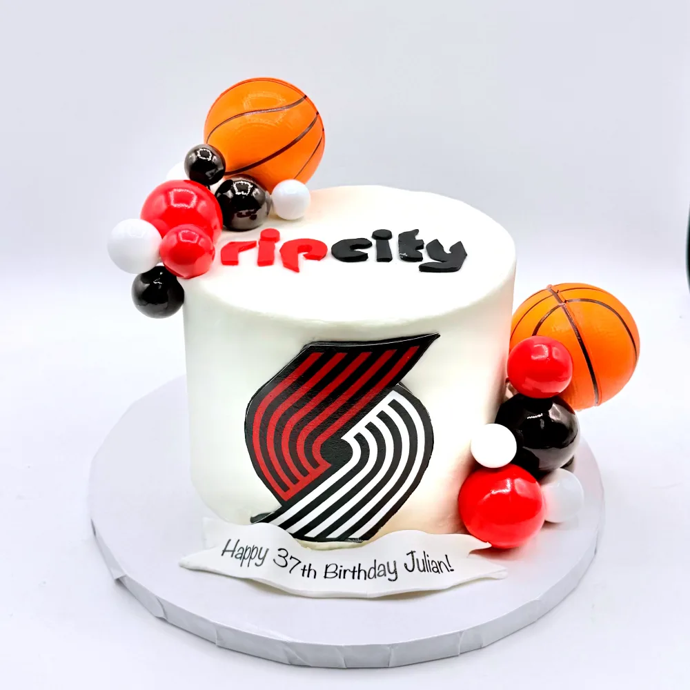 White cake with a Rip City Trail Blazers logo, basketballs and a red and black balloon cluster