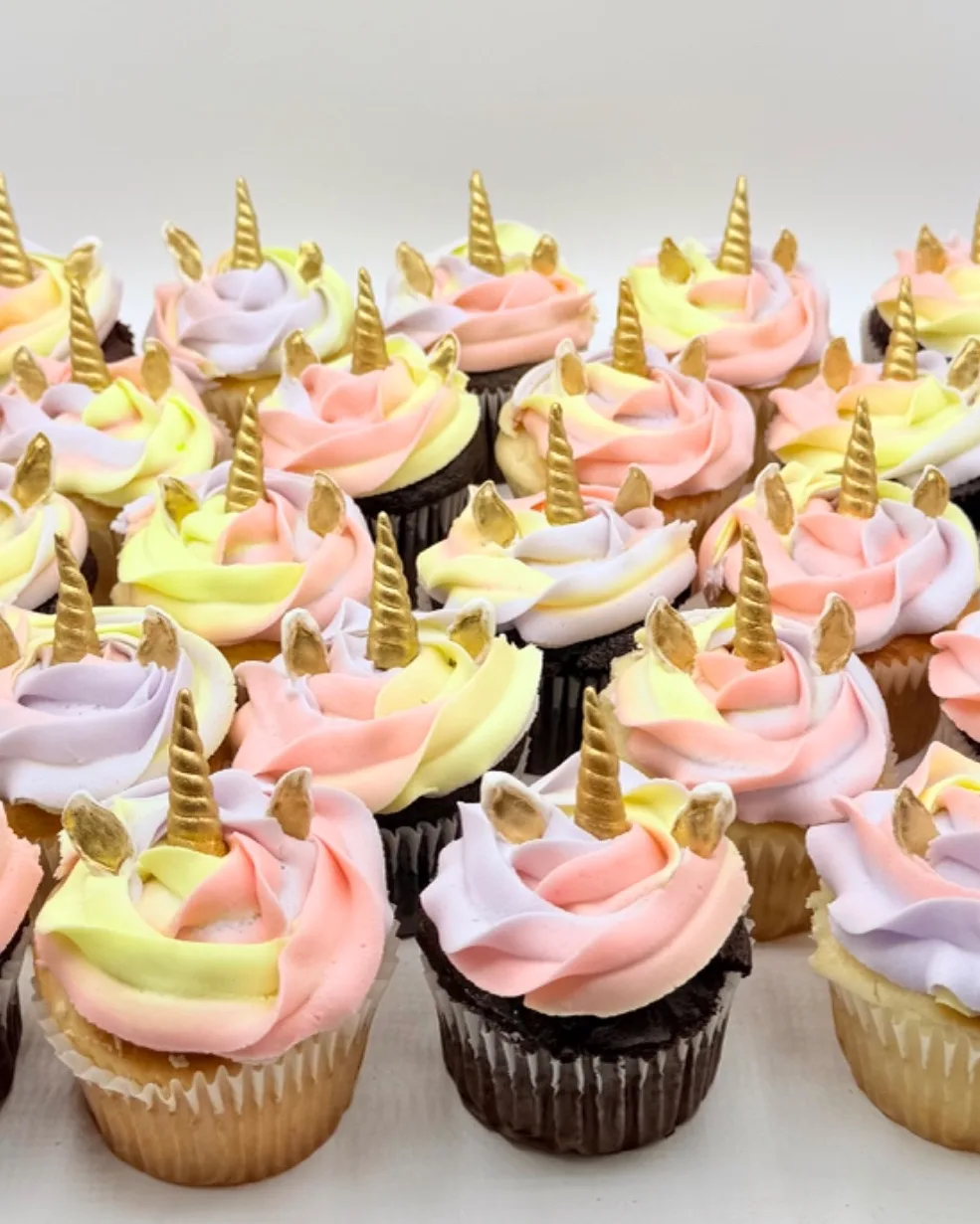 Rows of pastel pink, lavender, and mint buttercream swirl cupcakes, each topped with a gold fondant unicorn horn and ears.